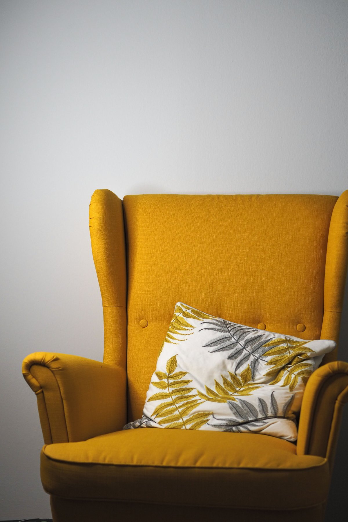 Stylish yellow armchair with a decorative leaf-patterned pillow against a gray wall.